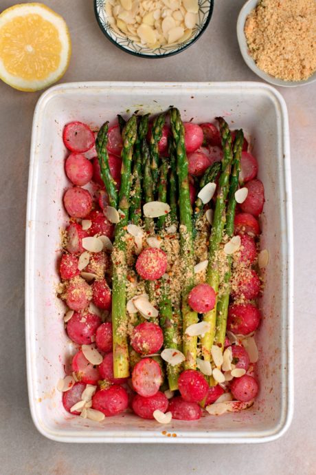 Asparagi sul letto di ravanelli arrostiti. Il tutto è ricoperto con parmigiano vegano e scaglie di mandorle.