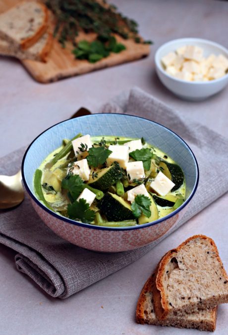 Ciotola con minestrone con zucchine e fagiolini decorato con cubetti di feta, foglioline di coriandolo e timo fresco